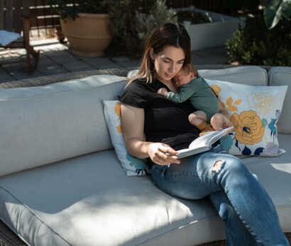 caucasian outside reading a book with a baby laying on her chest